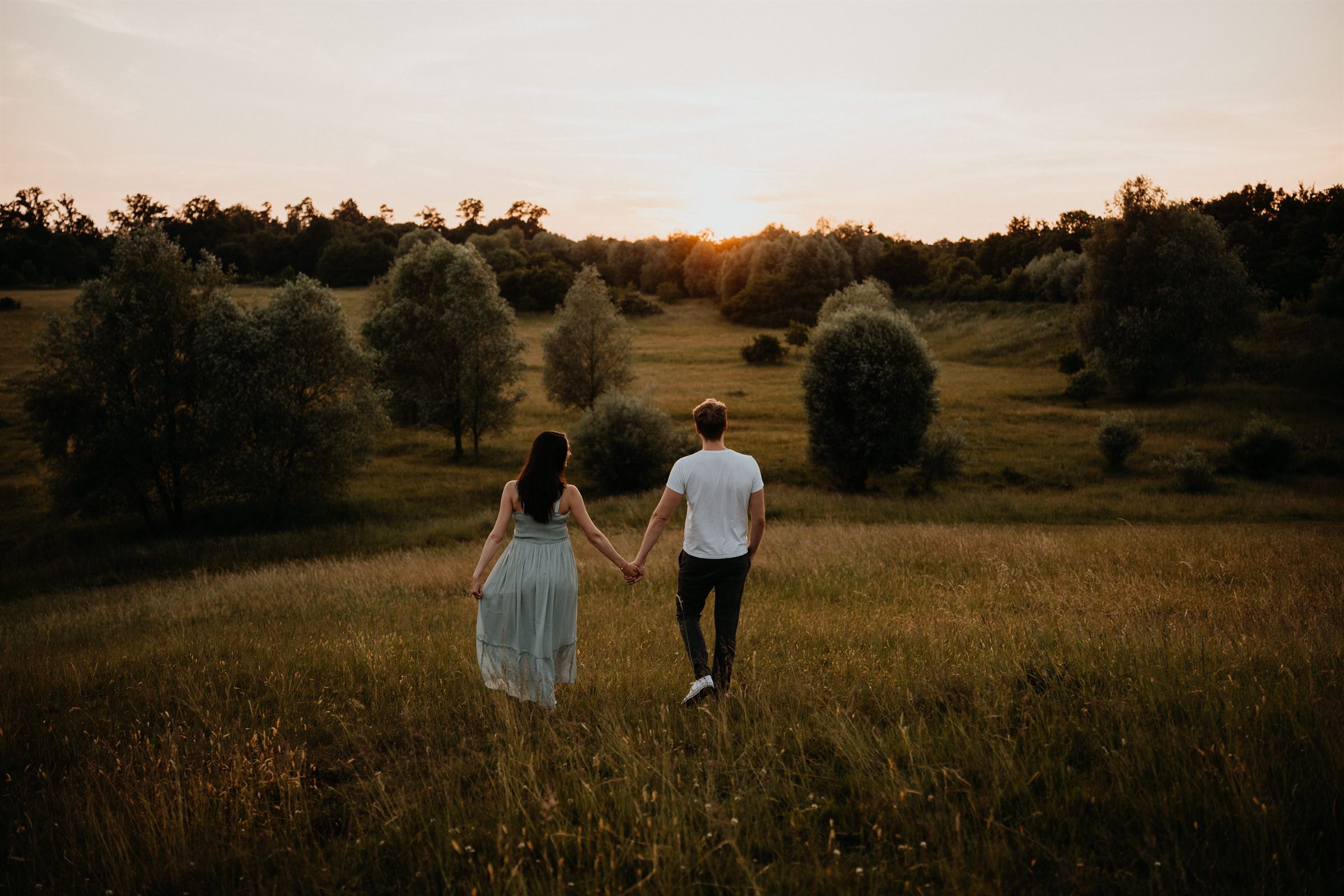Katrin und Martin gehen Hand in Hand über eine Wiese in den Sonnenuntergang
